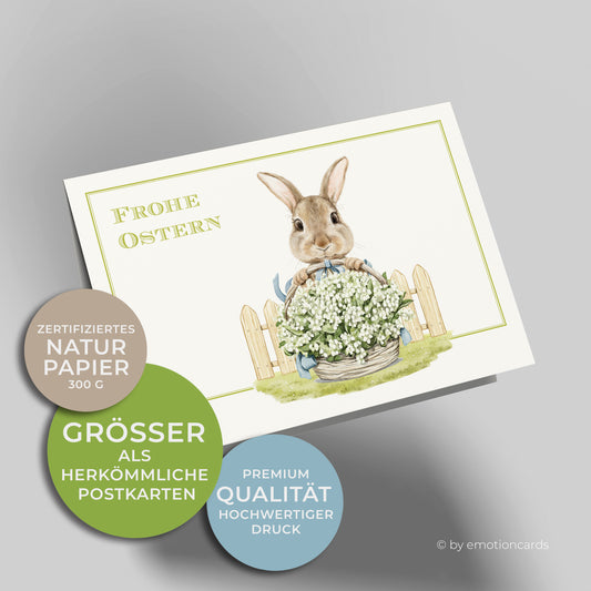 Osterkarte mit feinem grünen Doppelrahmen und kleiner Osterhase vor Gartenzaun, der einen großen Korb mit Maiglöckchen hält.