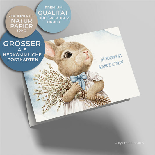 Süße Osterkarte mit hellblau wolkigem Hintergrund, kleiner Hase hält Weidenkätzchen Strauß im Arm.