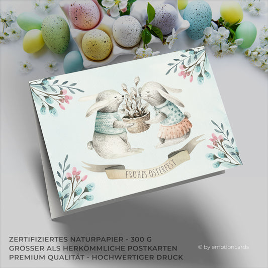 Osterkarte mit zwei Hasen die einen Korb mit Weidenkätzchen halten.