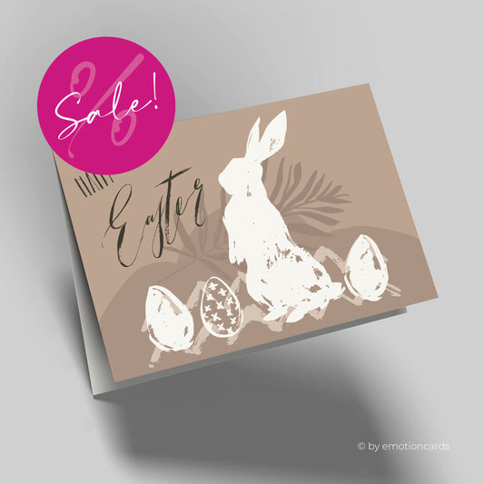 Moderne Osterkarte mit braunem Hintergrund, im Vordergrund ein weißer Osterhase mit 3 Eiern und in schwarz geschrieben Happy Easter