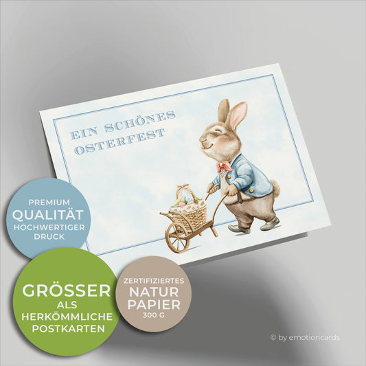 Süße Osterkarte im Querformat. Osterhase schiebt Schubkarre mit Osterkorb und Ostereiern, Wolkig hellblauer Hintergrund und feiner Doppelrahmen.