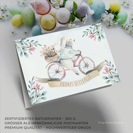 Osterkarte mit kleinem Hasen auf rotem Fahrrad und Korb mit Palmkätzchen auf dem Gepäckträger