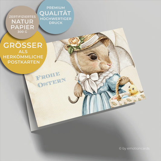 Osterkarte mit hellbraunem Hintergrund und Häsin mit Schirm und hellblauem Kleid trägt Osterkorb mit Eiern und kleinem gelben Küken darin.